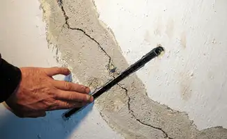 A wall with a large crack is being inspected by a professional in Kansas City, MO